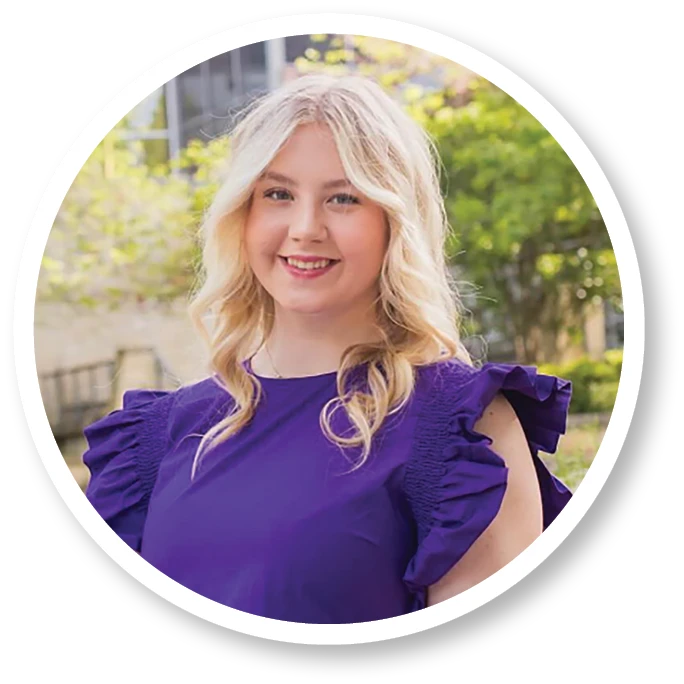 Portrait of a smiling young woman with long blonde hair wearing a purple top, standing outdoors on Abilene Christian University’s campus.