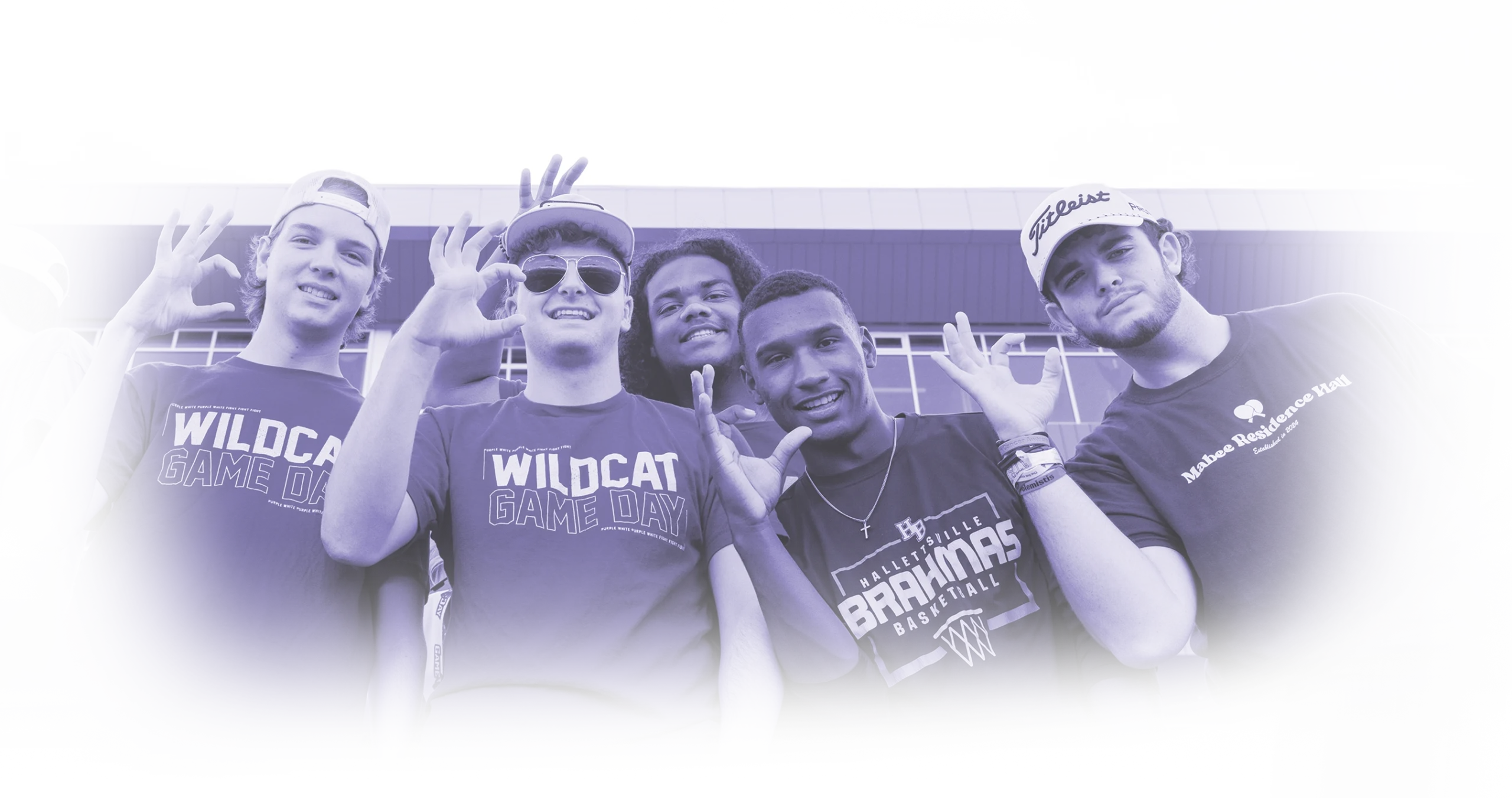 Stylized blue-toned photo of six young men smiling and posing outside a stadium, some wearing “Wildcat Game Day” shirts and making hand gestures. One wears a “Hallettsville Brahmas Basketball” shirt and another a “Mabee Residence Hall” shirt.