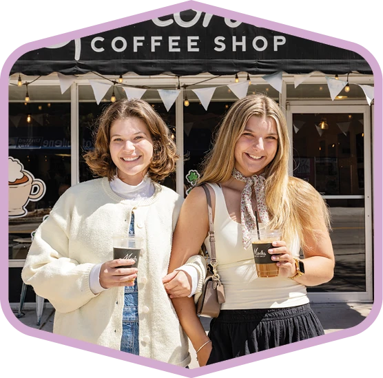 Two students hold drinks outside a local coffee shop.