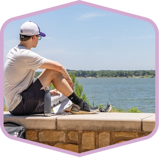Person sits beside the water at a park in Abilene.