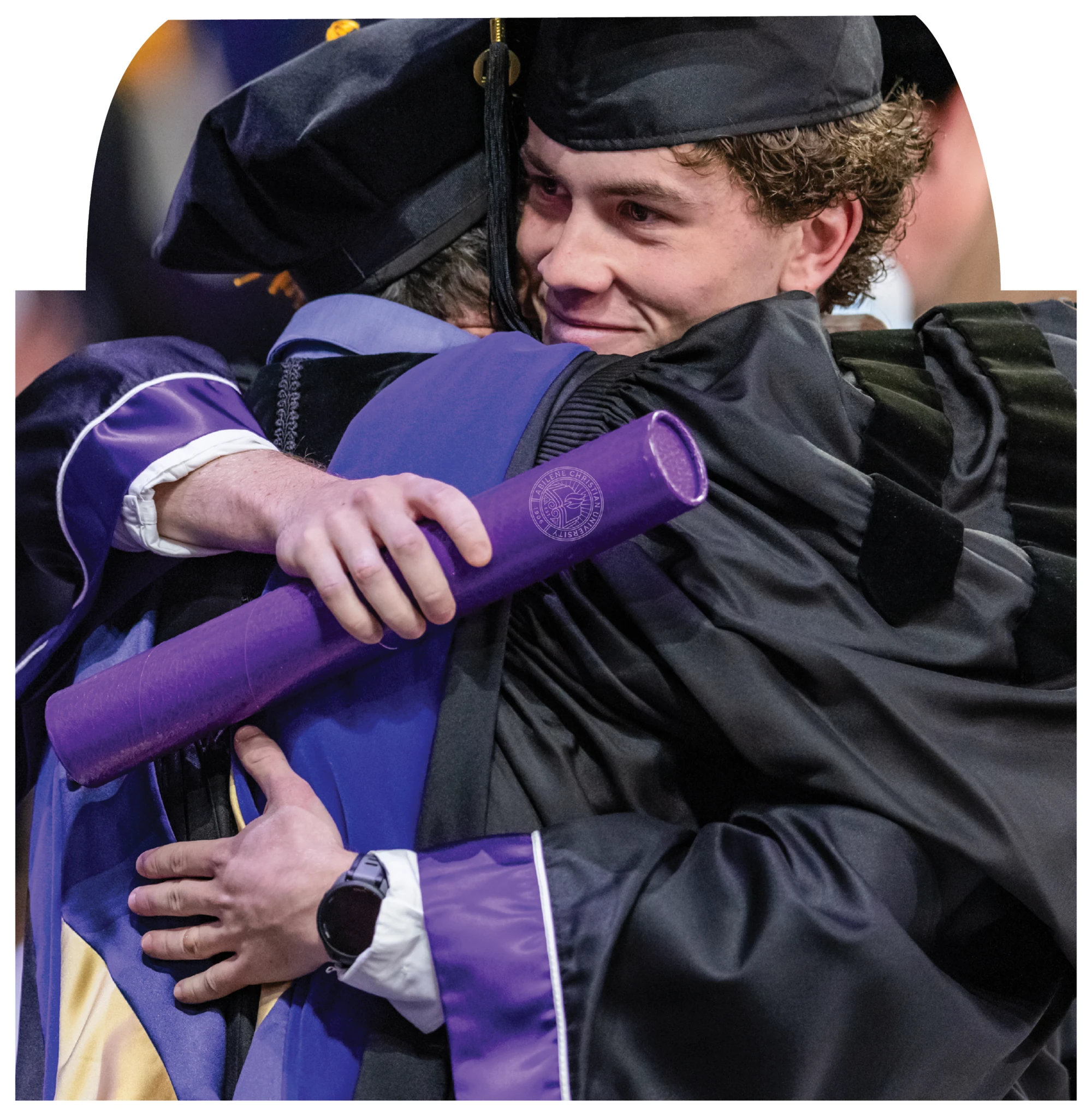 Graduate in academic regalia hugs another person after commencement.