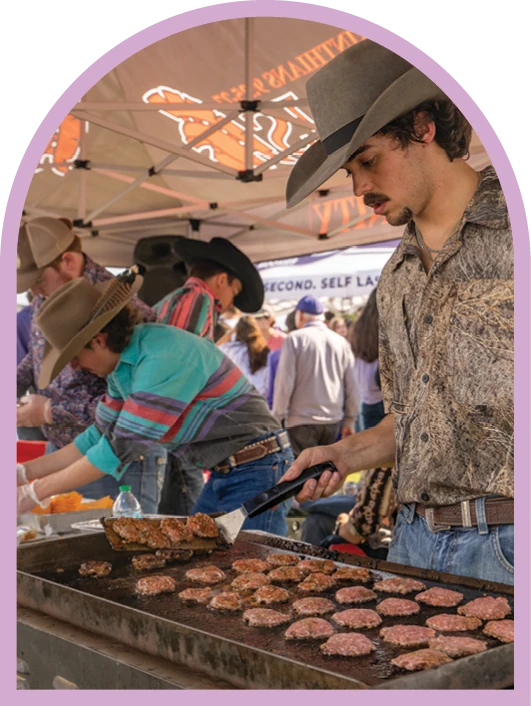 Students serving food at an ACU tailgate while wearing cowboy hats.