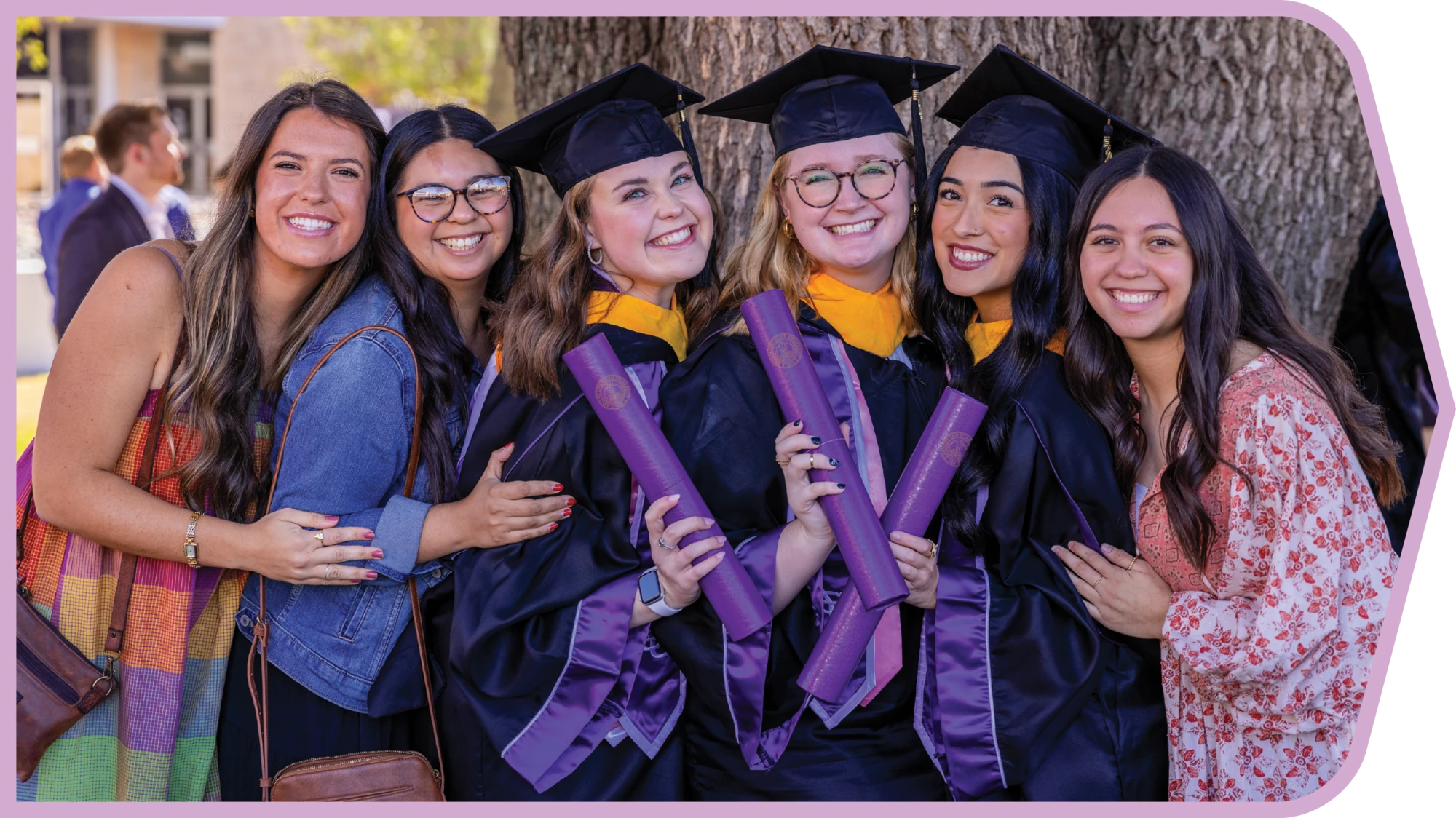 Group of ACU graduates smile together in caps and gowns.